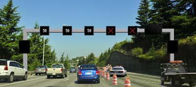 Graphic of an ATDM gantry with lanes closed. Three left lanes show 50 MPH reduced speed limit. Two right lanes show red X symbols for closed lanes. Image also shows construction barrels for lane closure.